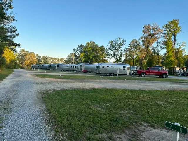 A row of silver Airstream trailers parked along a gravel campground road with a red pickup truck and tall trees.