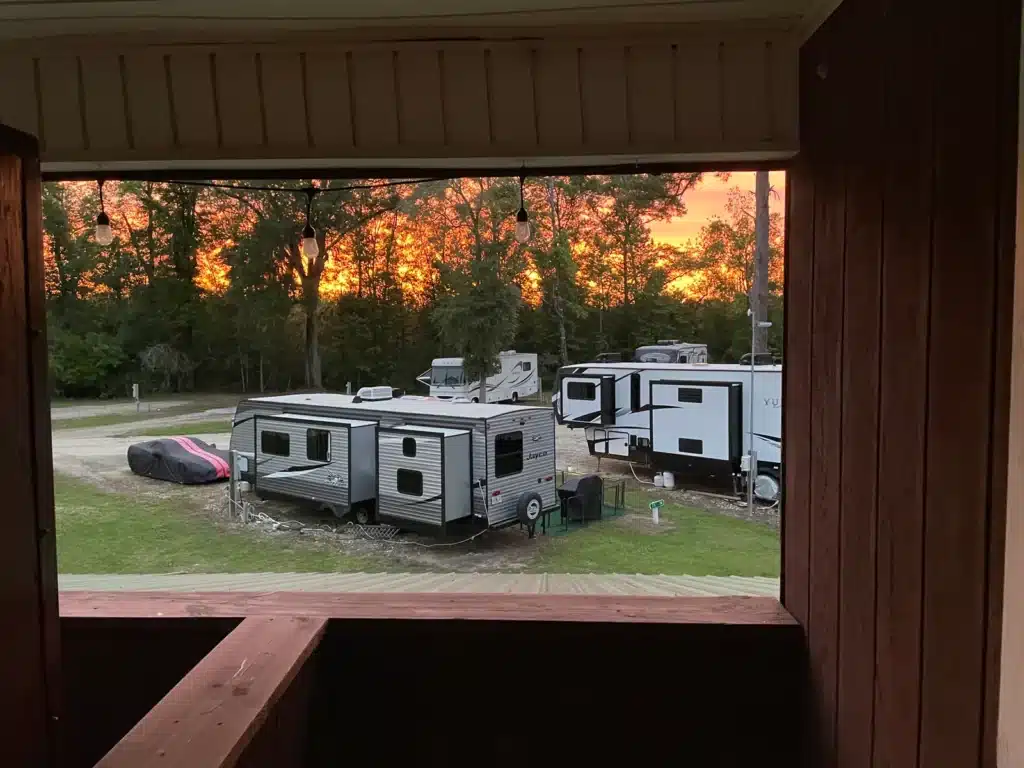 View from a covered cabin porch with string lights overlooking parked Jayco travel trailers and RVs at sunset.