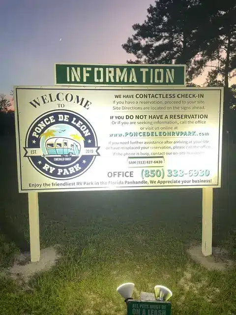 Photograph of Ponce de Leon RV Park's large white information sign at dusk, listing contactless check-in details and